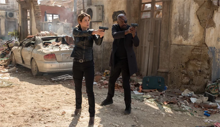 Maria Hill and Nick Fury stand in a ruined city in Mexico with their guns out.